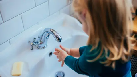 Getty Images A young girl with blonde hair washing her hands in a sink