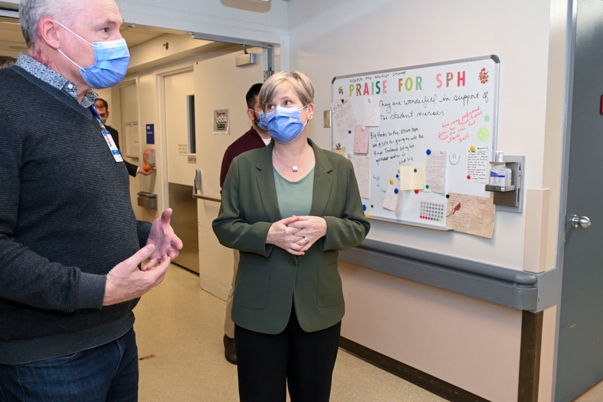 A man wearing a facemask in a hospital setting speaks to a woman who is also wearing a facemask.