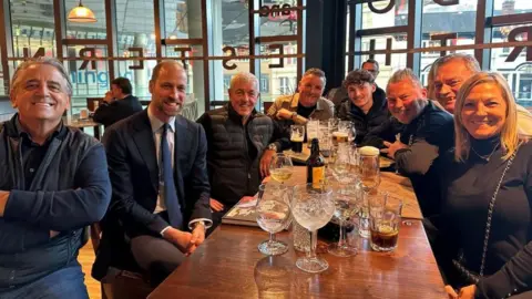 PA Media Prince William, second from the left, smiles alongside a group of Aston Villa fans around a table in Wetherspoon. Glasses of drinks are on the table