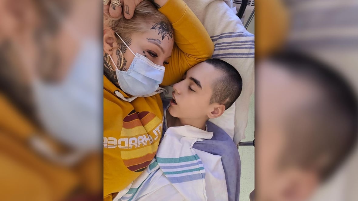 A woman wearing a mask lies in a hospital bed next to her son.