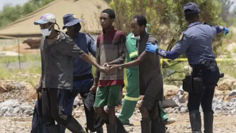 EPA Miners who have just resurfaced being led by police officers