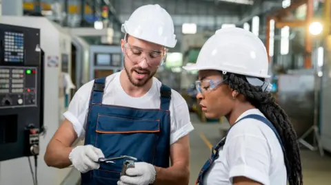 Getty Images Two engineers wearing white hard hats looking at a piece of equipment