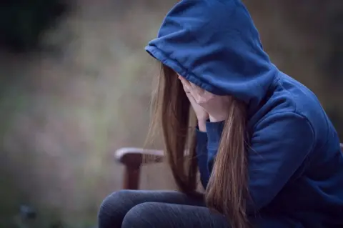 Getty Images A young girl with her head in her hands, wearing a blue hoodie that obscures her identity