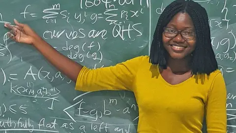 Angela Tabiri Angela Tabiri pointing at a blackboard with chalk calculations behind her