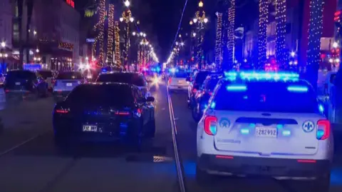 BBC Police cars with blue lights line the scene of the incident in New Orleans' French Quarter during night time hours 