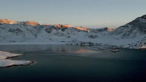 BBC A drone image of a fjord with snow covered mountains in the background