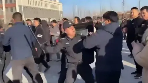 BBC A policeman beats a protester with a baton in Pucheng, Shaanxi province in China during large scale demonstrations. Grab from video on X