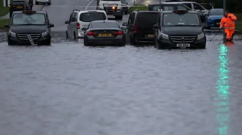 Reuters A council worker attempts to unblock drains after heavy overnight rain caused roads to flood, leaving cars stranded in Manchester