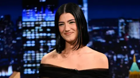 Getty Images A woman with straight black hair smiles. She is in the studio of the Jimmy Fallon show.