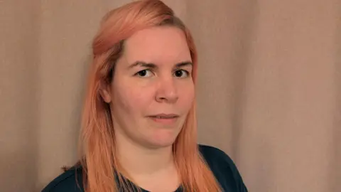 Anna Malnutt Woman in her thirties with long strawberry blonde hair and a pensive look on her face